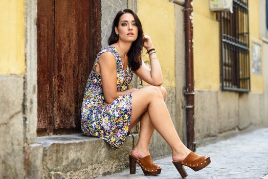 Beautiful young woman with blue eyes sitting on urban step. Girl wearing flower dress outdoors. Beauty and fashion concept.