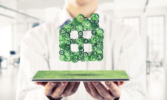 Close of businessman holding tablet pc with house sign made of connected gears. Mixed media