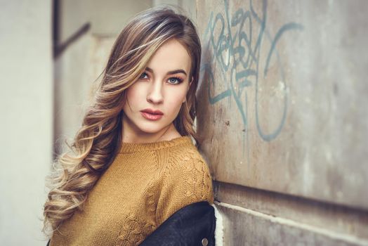 Blonde woman in urban background. Beautiful young girl wearing black leather jacket and mini skirt standing in the street. Pretty russian female with long wavy hair hairstyle and blue eyes.