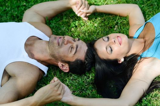 Happy smiling couple laying on green grass in a beautiful park