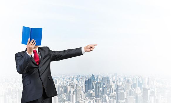 Businessman covered his face with organizer and finger pointing side. Man in business suit and tie standing on cityscape background. Education and professional knowledges. Direction and instruction.