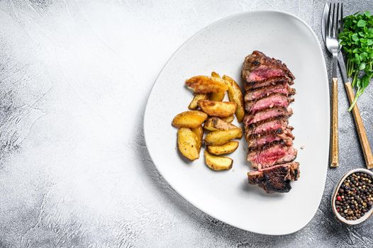 Sliced striploin steak with potato. White background. Top view. Copy space.