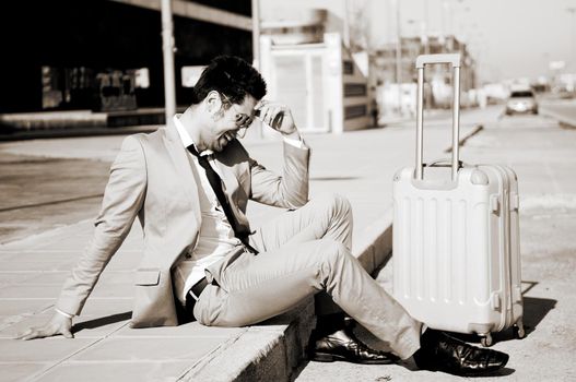 Man dressed in suit and suitcase sitting on the floor in the street