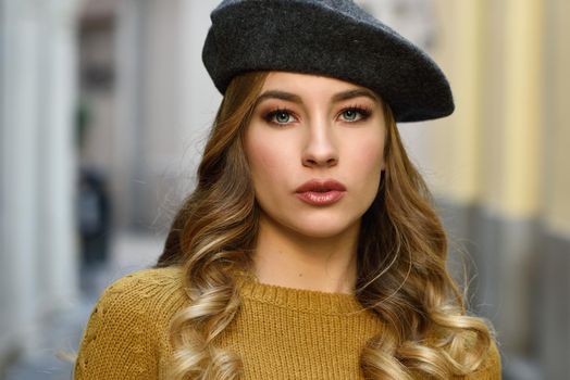 Blonde russian woman in urban background. Beautiful young girl wearing beret, black leather jacket and mini skirt standing in the street. Pretty female with long wavy hair hairstyle and blue eyes.
