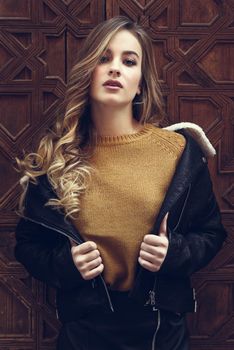 Blonde woman in urban background. Beautiful young girl wearing black leather jacket and mini skirt standing in the street. Pretty russian female with long wavy hair hairstyle and blue eyes.