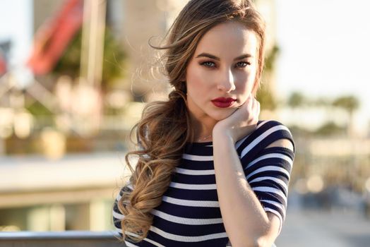 Blonde woman, model of fashion, standing in urban background. Beautiful young girl wearing striped t-shirt and blue jeans in the street. Pretty russian female with pigtai and blue eyes.