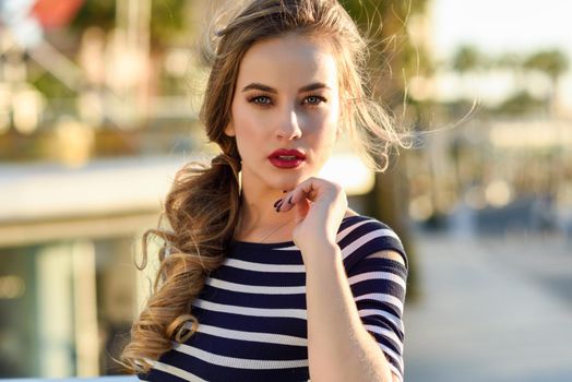 Blonde woman, model of fashion, standing in urban background. Beautiful young girl wearing striped t-shirt and blue jeans in the street. Pretty russian female with pigtai and blue eyes.