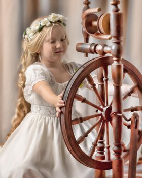 A cute little girl wove a wool with a rotating wheel. Retro style, memories of the past.