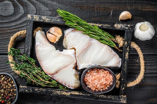 Shark raw fish steaks in a wooden tray with herbs. Black wooden background. Top view.