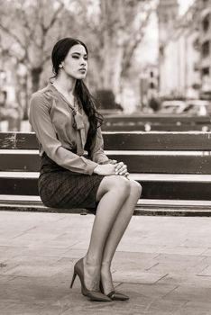 Portrait of hispanic bussinesswoman in urban background wearing red shirt and skirt sitting on a bench in the street