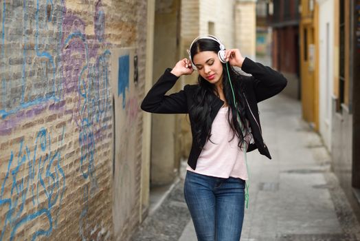 Portrait of young dominican woman in urban background listening to music with headphones