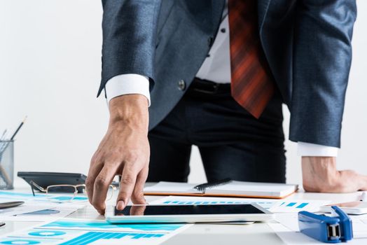 Businessman standing near office desk and using tablet computer. Banking and financial management. Corporate manager in suit and tie working with business analytics. Entrepreneurship and leadership.