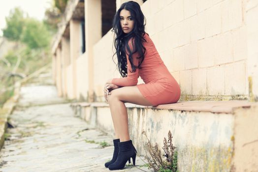 Portrait of hispanic young woman wearing casual orange dress in urban background