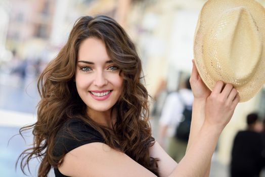 Happy young woman with blue eyes smiling in urban background. Girl wearing summer clothes and sun hat.