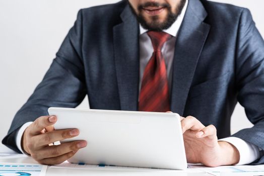 Businessman using tablet computer at office desk. Financial expertise and consulting. Manager in suit and tie sitting at desk with documents and tablet computer. Corporate accounting and paperwork