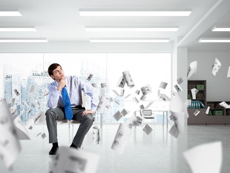 young businessman sits on an office chair. thoughtful and looking up. documents fly around