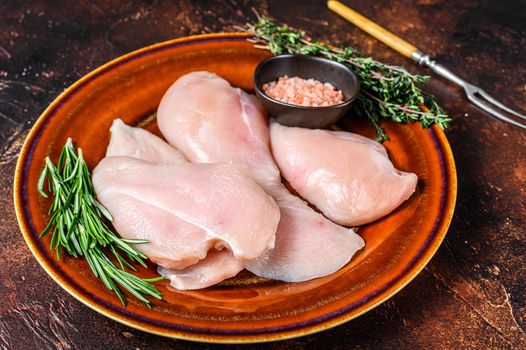 Raw slices of chicken breast fillet steaks on a rustic plate with herbs. Dark background. Top view.