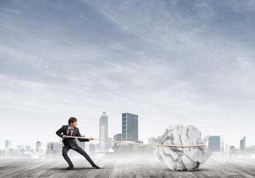 Young businessman outdoors making huge paper ball move