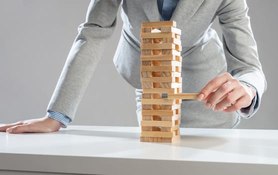 Businesswoman removing wooden block from tower on table. Management of risks concept with wooden boxes game. Business development and assistance. New challenge and leadership motivation.