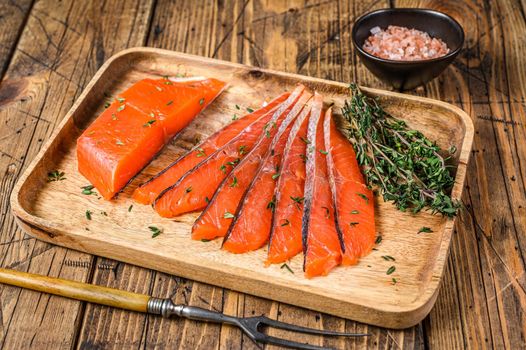 Salted salmon fillet slices in a wooden tray with thyme. wooden background. Top view.