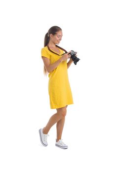 Full length side view of a beautiful female photographer looking pictures at camera over white background