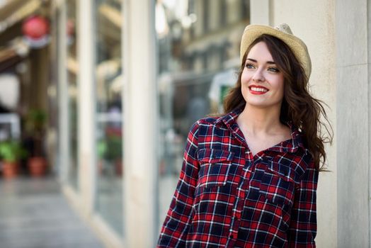 Young woman with beautiful blue eyes wearing plaid shirt and sun hat. Girl smiling in urban background.