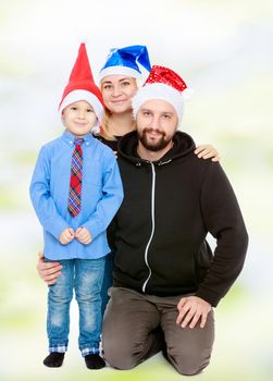 Happy family of 3 people in caps of Santa Claus, the Christmas tree and the fireplace in the Christmas night.