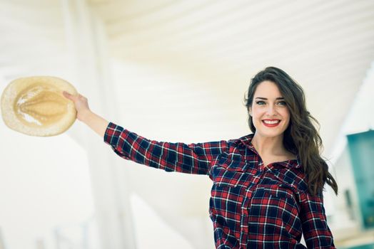 Young woman with beautiful blue eyes wearing plaid shirt and sun hat. Girl smiling in urban background.