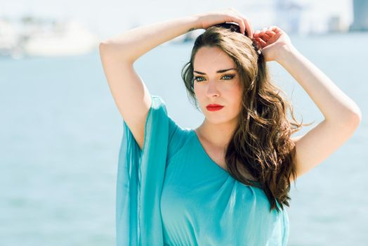 Beautiful young woman with blue eyes wearing blue dress in the beach.