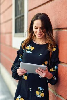 Young woman using digital tablet outdoors. Female in casual clothes with care hair in Granada, Andalusia, Spain.