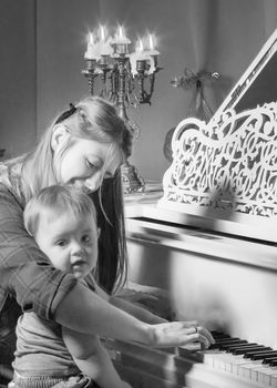 A young mother with a small child on Christmas night with candles near a large white piano. The concept of holidays and family happiness.