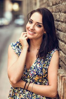 Girl with blue eyes smiling on brick wall. Happy woman wearing flower dress in urban background.