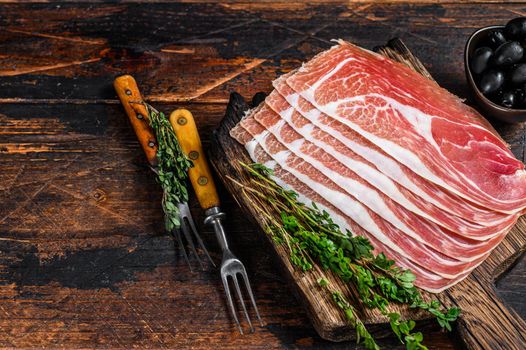 Traditional Spanish sliced Jamon Serrano ham on a cutting board. Dark wooden background. Top view. Copy space.