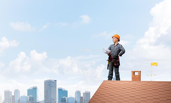 Builder in hardhat with technical blueprints. Young female architect in shirt and jeans standing on brick roof of house. Professional success and new horizons. Renovation and roofing construction.
