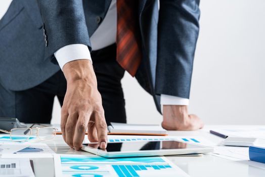 Businessman standing near office desk and using tablet computer. Banking and financial management. Corporate manager in suit and tie working with business analytics. Entrepreneurship and leadership.