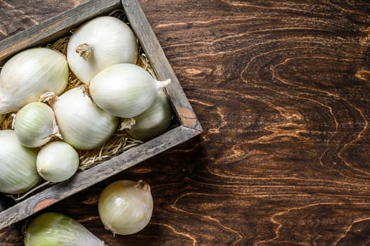 Raw fresh white onion in wooden box. Wooden background. Top view. Copy space.