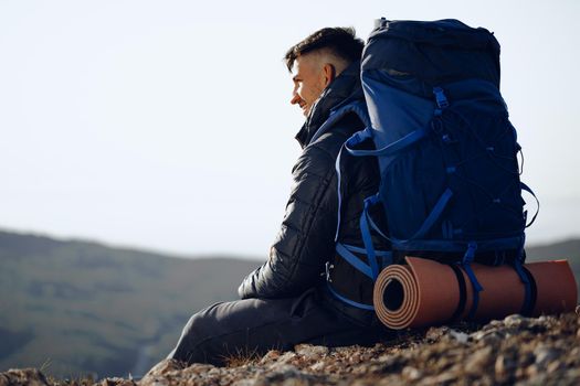 Young male hiker sitting and having a rest on a halt stop in mountains
