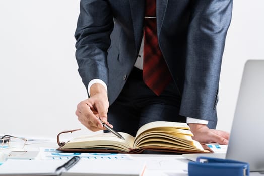 Businessman analyzing financial documents at office desk. Financial expertise and consulting. Manager in suit and tie planning day with personal organizer. Time management and work organization.