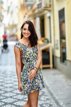 Smiling young woman with blue eyes with brown wavy hair outdoors. Girl wearing flower dress in urban background. Beauty and fashion concept.