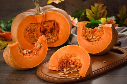  Whole fresh orange big pumpkin and slice of pumpkin on wooden board, closeup. Organic vegetable product, ingredients for cooking, healthy food vegan