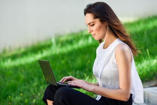 Middle-age businesswoman working with her laptop computer sitting on urban steps outdoors.