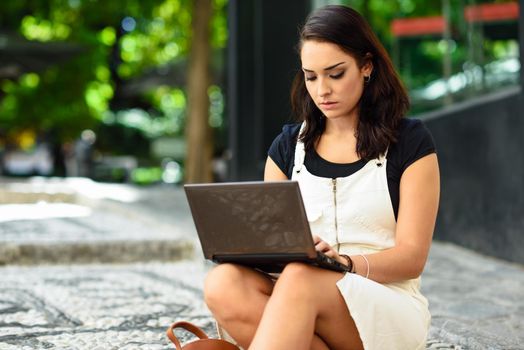 Beautiful young woman using laptop computer sitting on urban steps. Businesswoman wearing casual clothes working outdoors. Lifestyle concept.