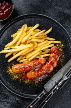 German currywurst Sausages with French fries on a plate. Black background. Top view.