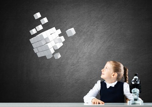 Little girl scientist with microscope on chalkboard background with flying 3d cubes. Research and discovery concept. Elementary science class in modern school. Schoolgirl in schoolwear sitting at desk