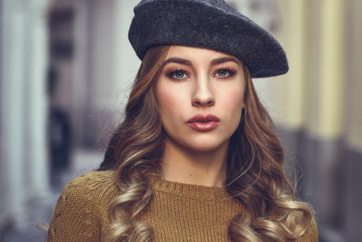 Blonde russian woman in urban background. Beautiful young girl wearing beret, black leather jacket and mini skirt standing in the street. Pretty female with long wavy hair hairstyle and blue eyes.