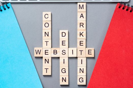 Web marketing concept with words from cubes. Still life of office workplace with crossword. Flat lay grey surface with spiral notebooks. New strategy planning and workflow optimization.