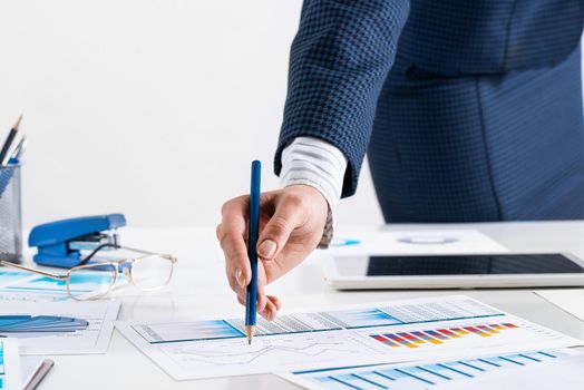 Businesswoman standing near office desk and analyzing financial charts. Successful corporate manager in business suit. Close-up woman hand with pen. Business presentation in conference room