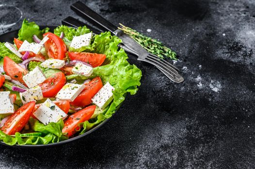 Fresh Greek salad with vegetables and feta cheese in a plate. Black background. Top view. Copy space.