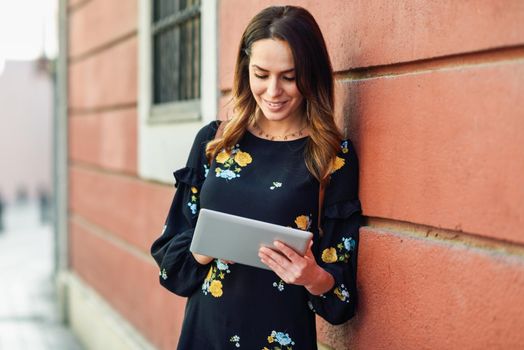 Young woman using digital tablet outdoors. Female in casual clothes with care hair in Granada, Andalusia, Spain.