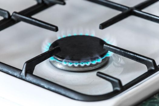 Gas burner with a blue flame on a gas stove, close-up.